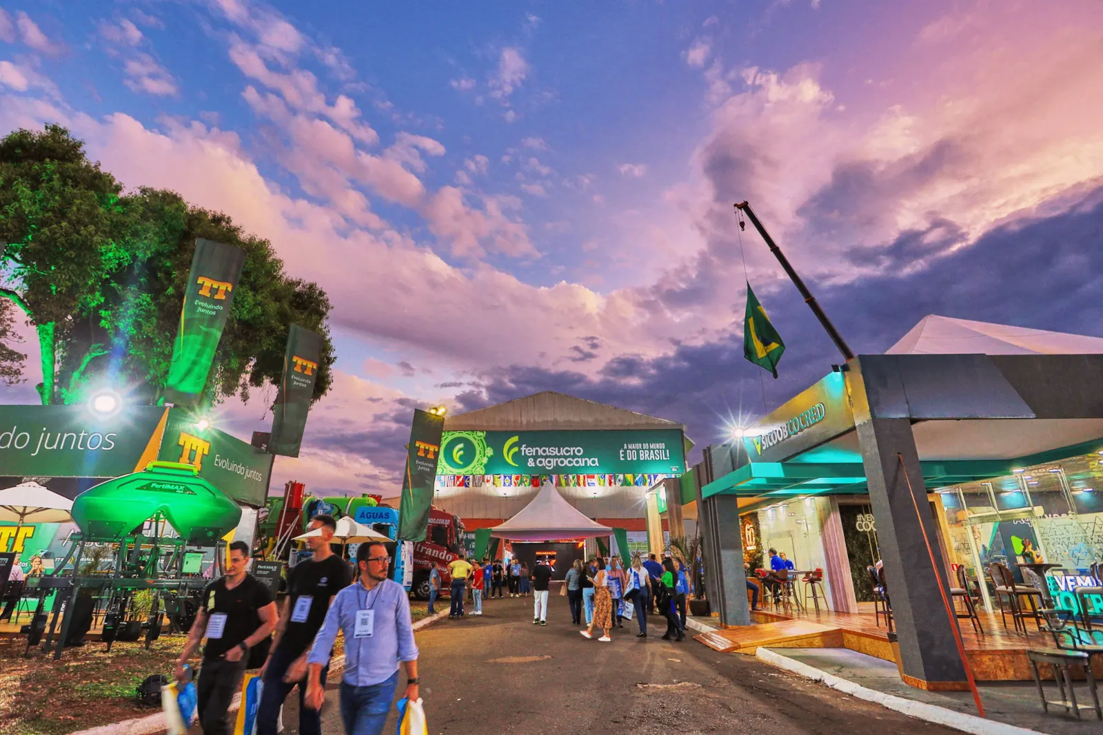Entrada da Fenasucro & Agrocana ao entardecer, com expositores, bandeiras e visitantes circulando pelo pavilhão em Sertãozinho