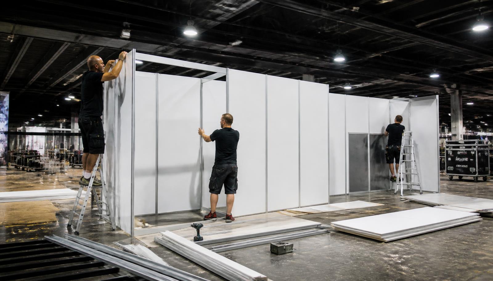 Equipe montando estrutura modular em Octanorm para camarins dentro de pavilhão de eventos
