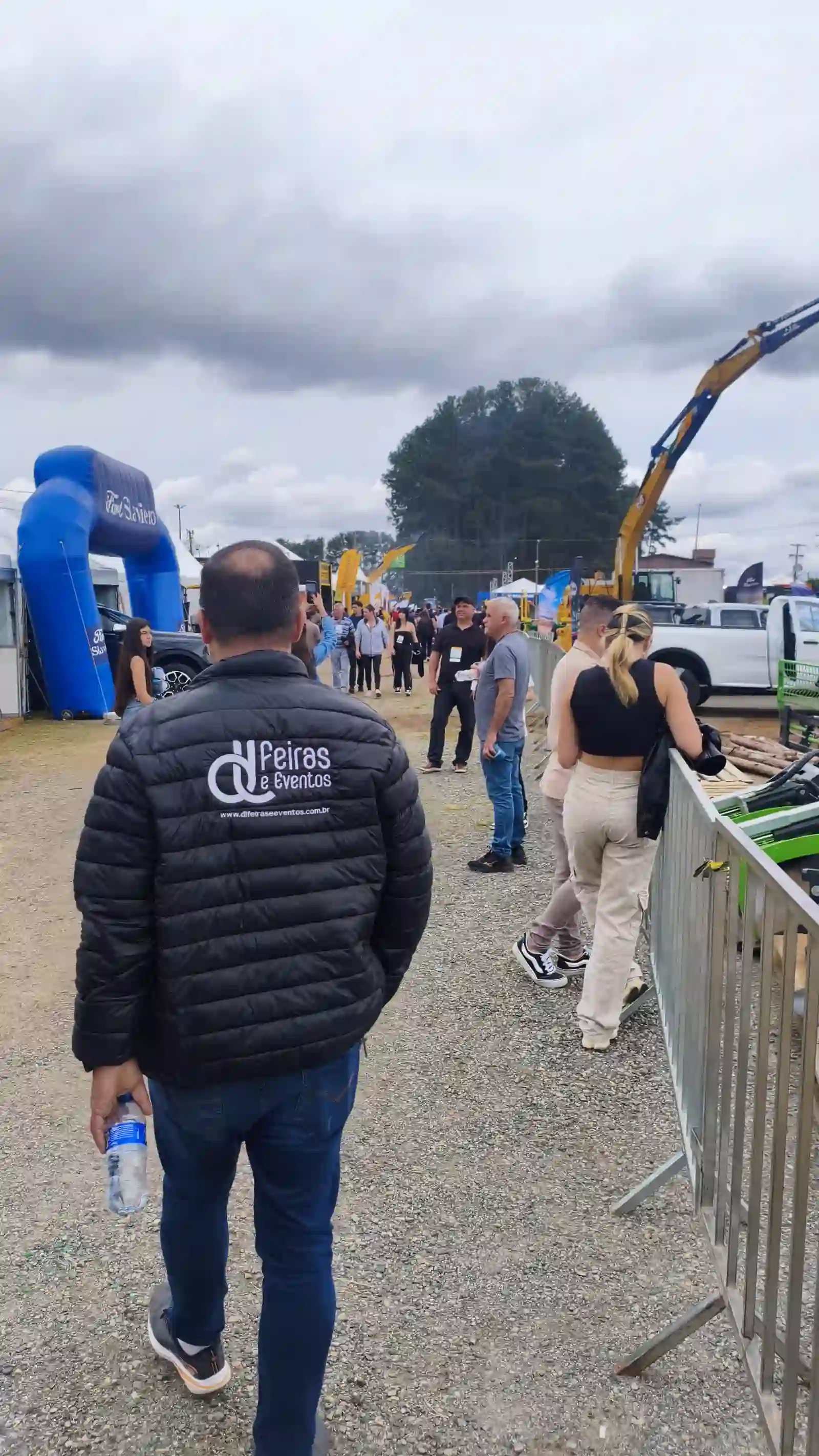 Público circulando pela Arena M&T 2026 entre stands e máquinas em demonstração, com integrante da equipe DL Feiras e Eventos em primeiro plano