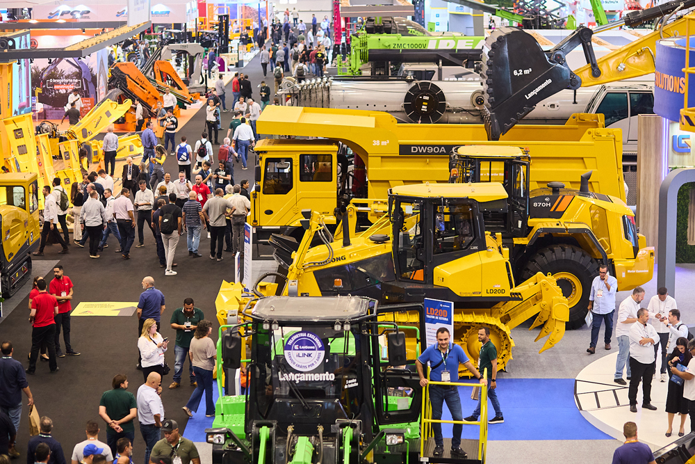 Vista aérea de pavilhão da M&T Expo com estandes de fabricantes de máquinas amarelas, caminhões fora de estrada e público circulando