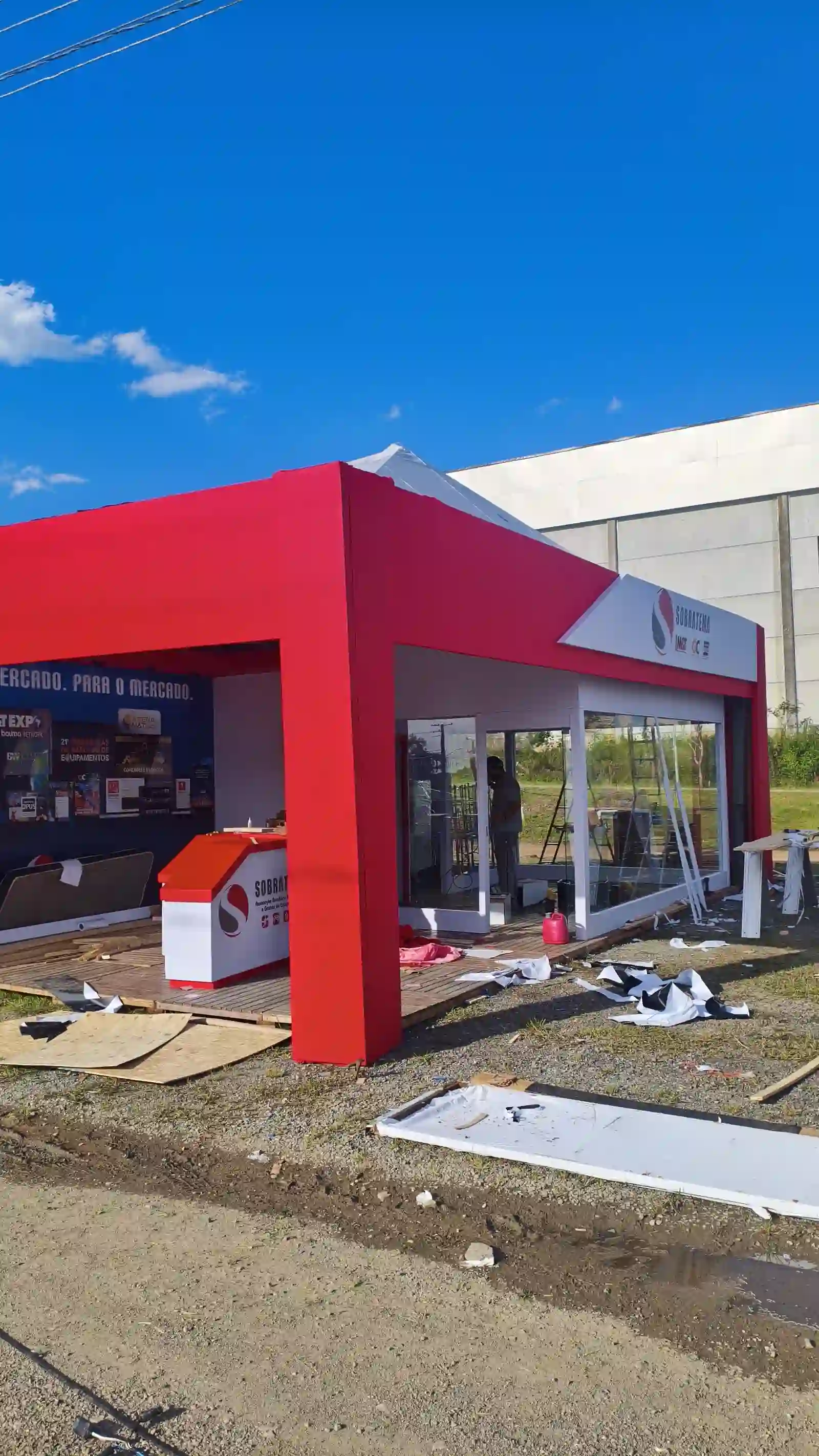 Equipe da DL Feiras e Eventos montando o estande da Sobratema na Arena M&T 2026, com escadas, painéis vermelhos e balcões em fase de acabamento