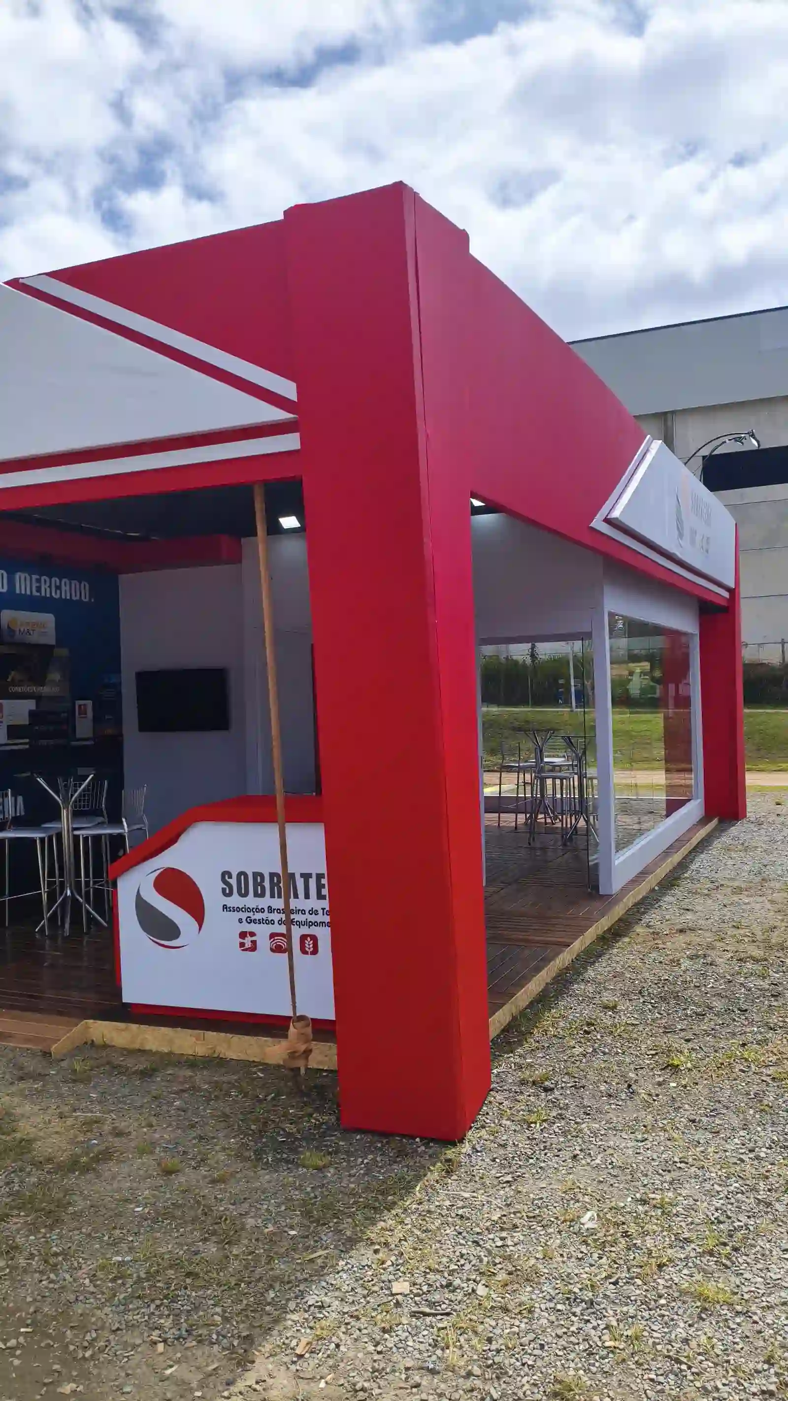 Estande construído da Sobratema pronto na Arena M&T 2026, com fachada vermelha, envidraçamento, deck de madeira e balcão de atendimento