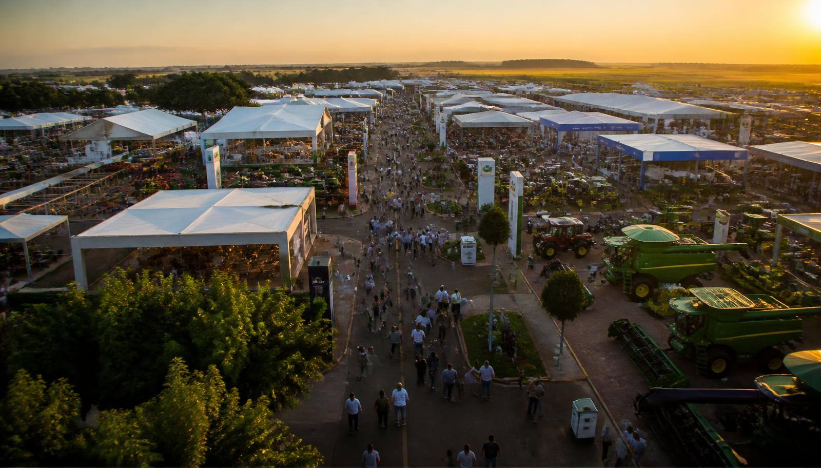 Alameda do Show Rural ao entardecer com fileiras de tendas, colheitadeiras em exposição e grande público