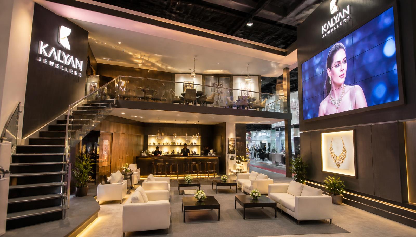 Interior de stand construído com mezanino, lounge de sofás, bar de café, painel de LED e escada com guarda-corpo de vidro