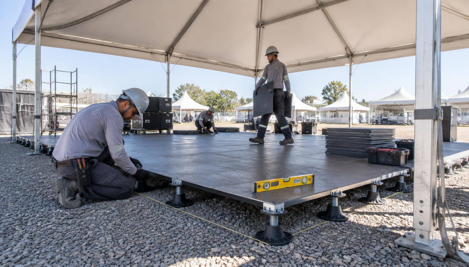 Equipe técnica instalando e nivelando piso elevado sob tenda em área de brita